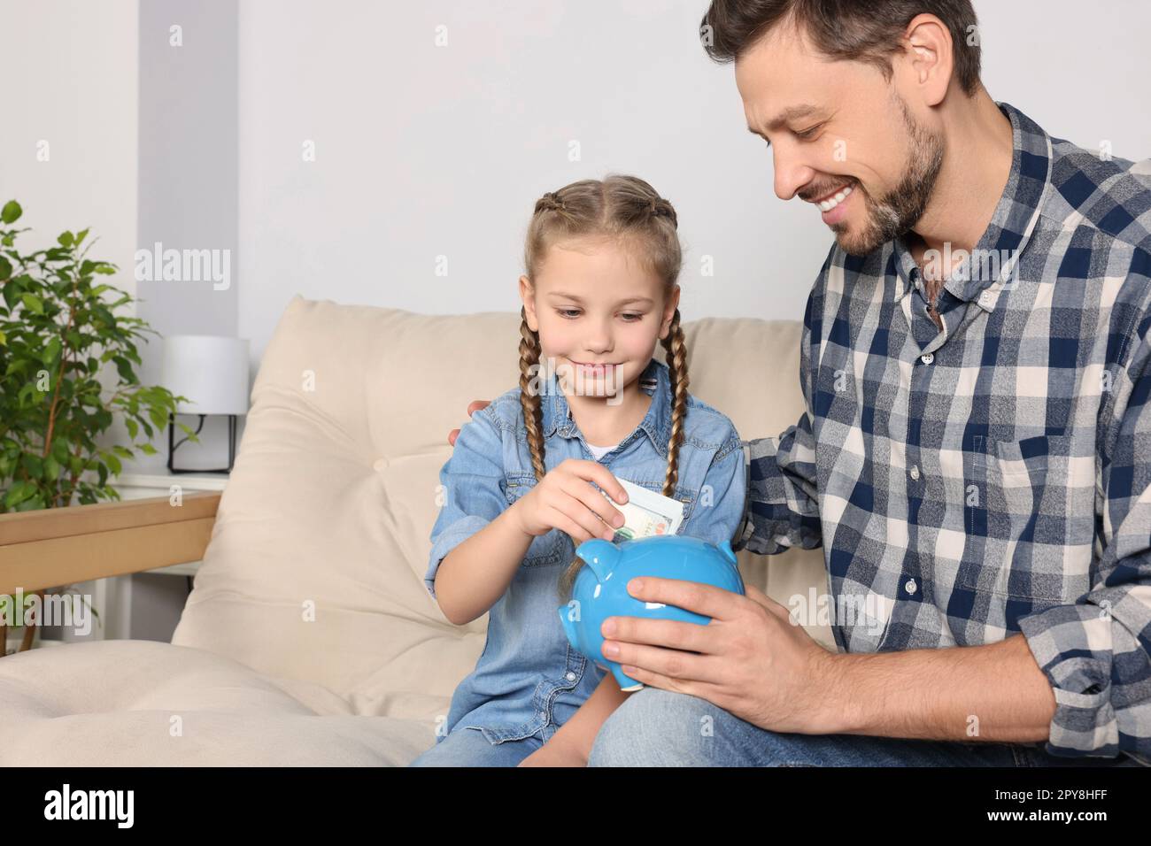 Little girl with her father putting money into piggy bank at home Stock ...