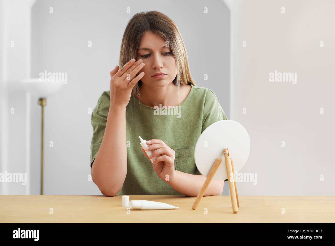 Sleep deprived young woman covering up dark circles with concealer near