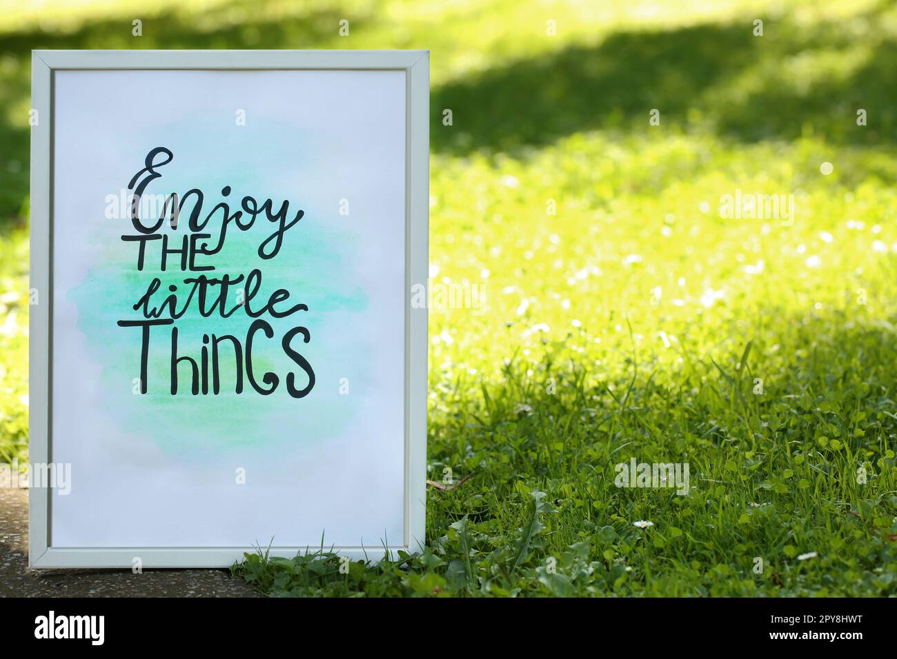 Poster with phrase Enjoy The Little Things on grass outdoors, space for text Stock Photo