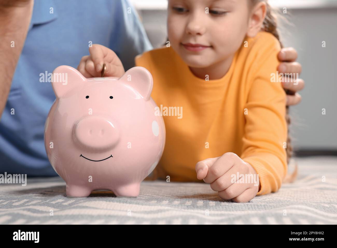 Little girl with her father putting coin into piggy bank at home ...