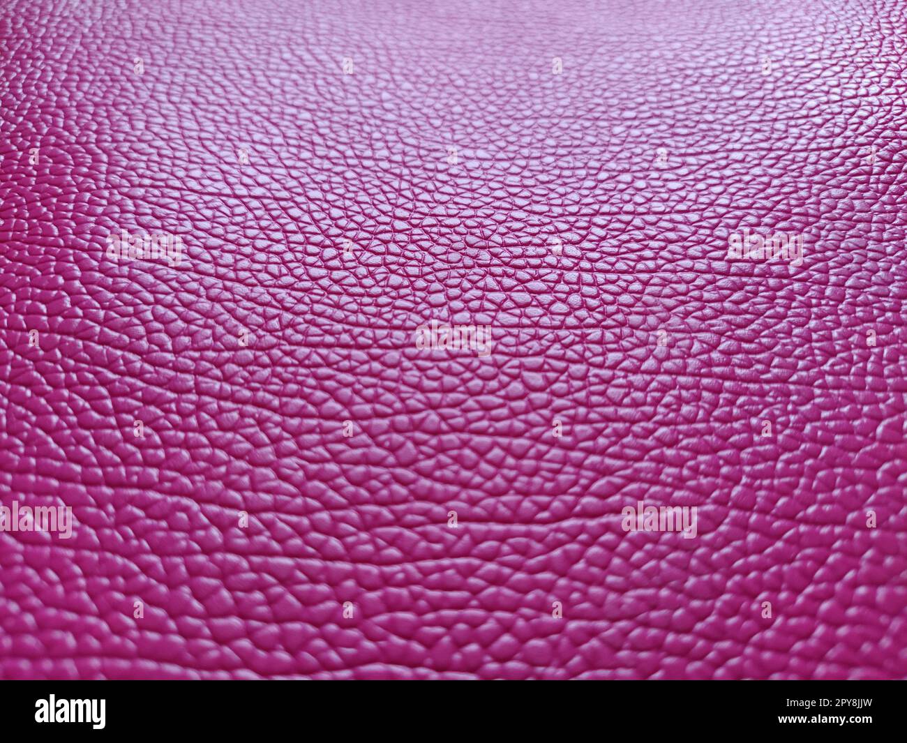 Artificial leather is bright pink or fuchsia. Distinct furrows and elevations on the surface of a bag or shoe. Reflection of the light. Fashion accessory made of imitation pig skin. Close-up Stock Photo