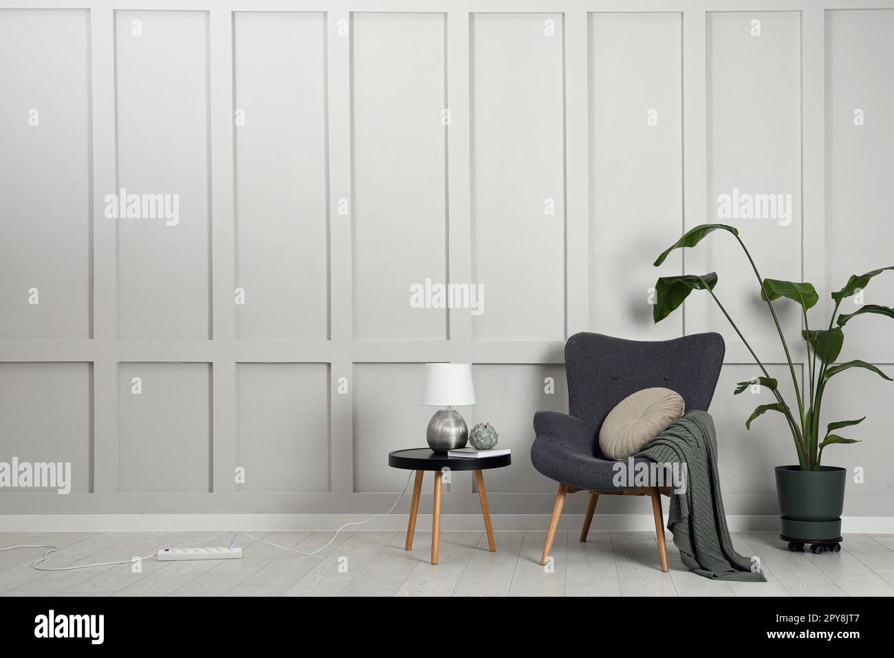 Comfortable armchair, table with lamp and houseplant near light grey ...