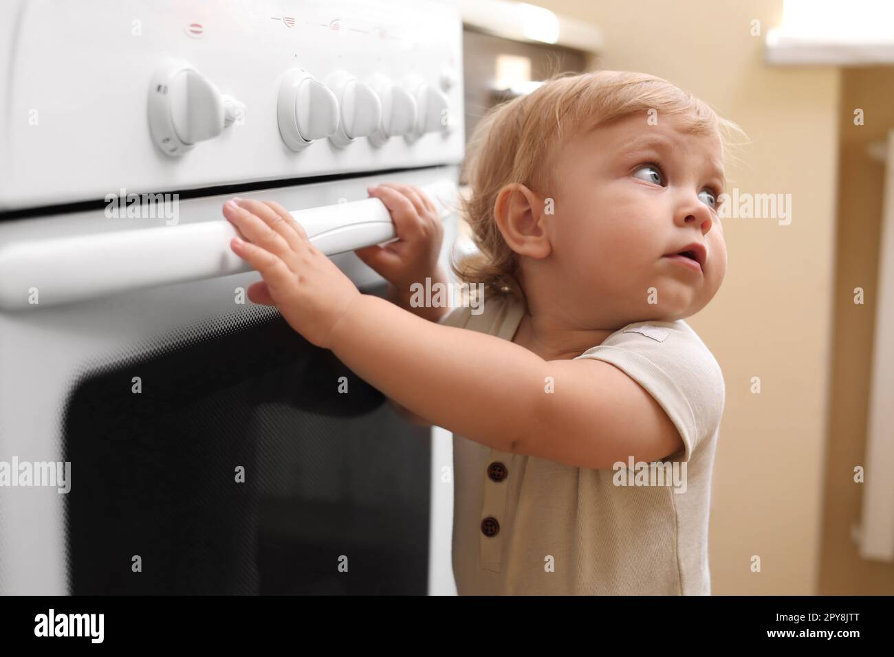 Little child playing with gas stove indoors. Dangers in kitchen Stock