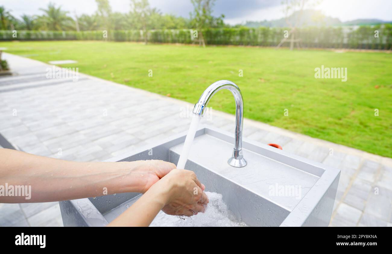 World water day concept. Woman washing hands with tap water under faucet at white sink. Washing hands with tap water at outdoor sink near green grass lawn. Personal hygiene. Water consumption. Stock Photo