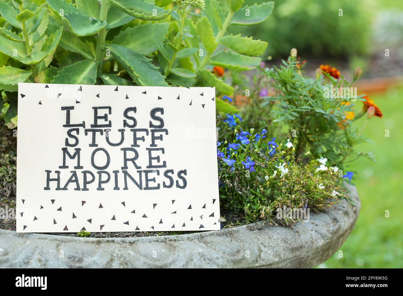 Card with phrase Less Stuff More Happiness on stone planter outdoors Stock Photo