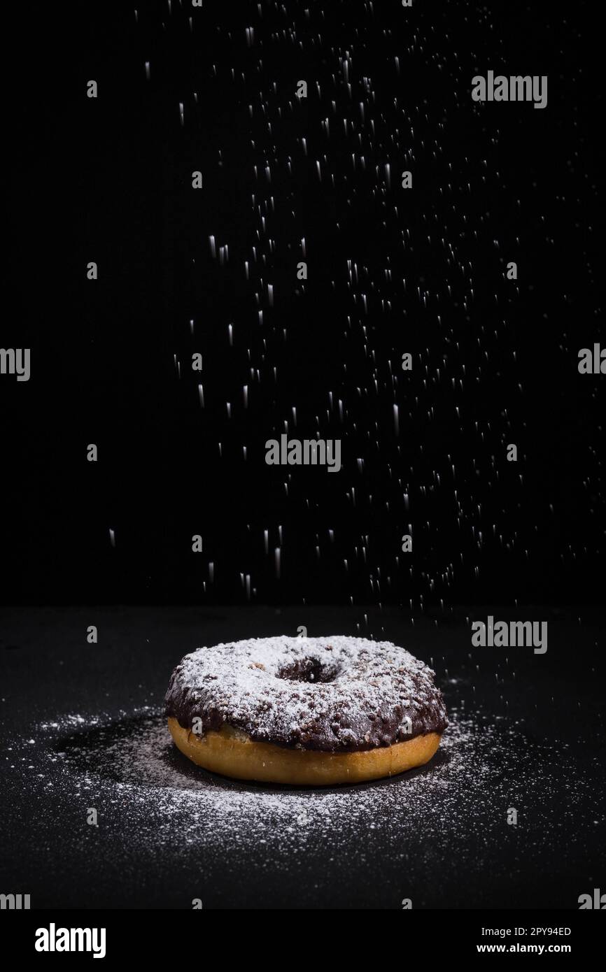 Sprinkling sugar powder on chocolate donut Stock Photo