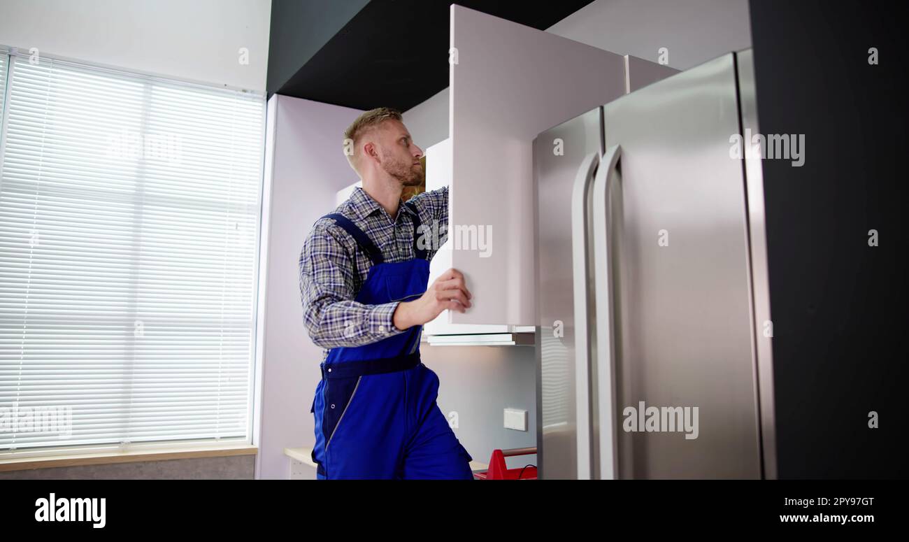 Male Carpenter Assembling White Cabinet On Wall Stock Photo