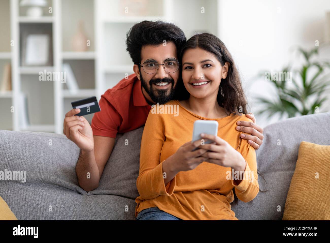 Happy young indian couple using smartphone and credit card at home ...