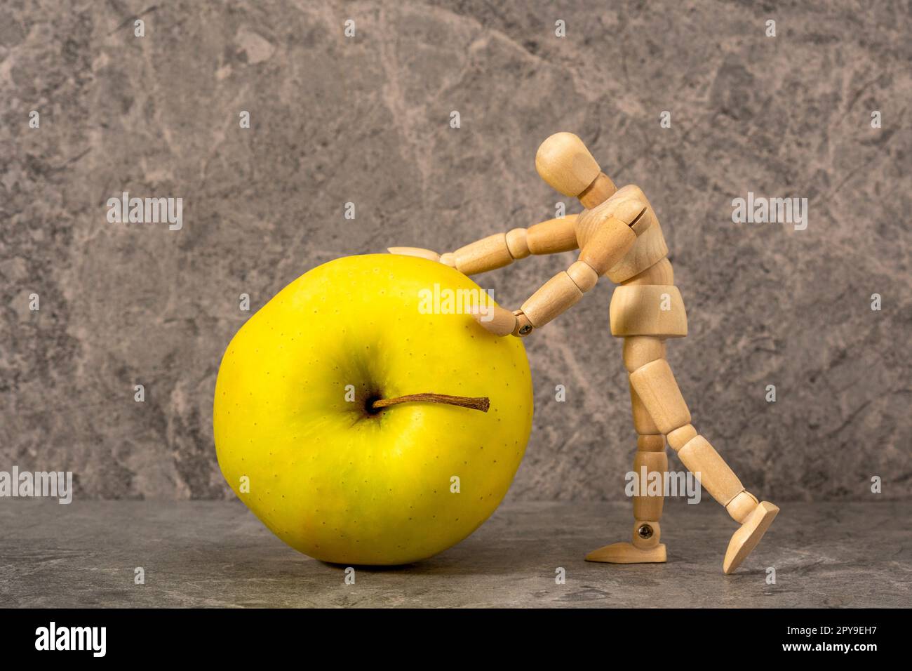 Wooden mannequin rolling green apple along grey concrete background Stock Photo