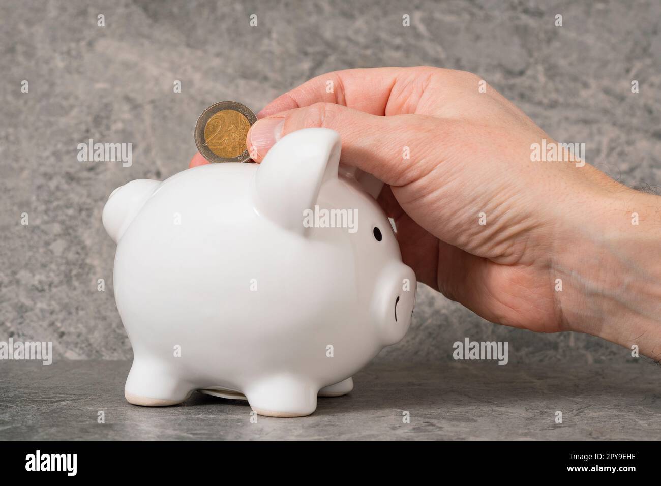 Hand putting 2 euro coin to piggy bank Stock Photo - Alamy