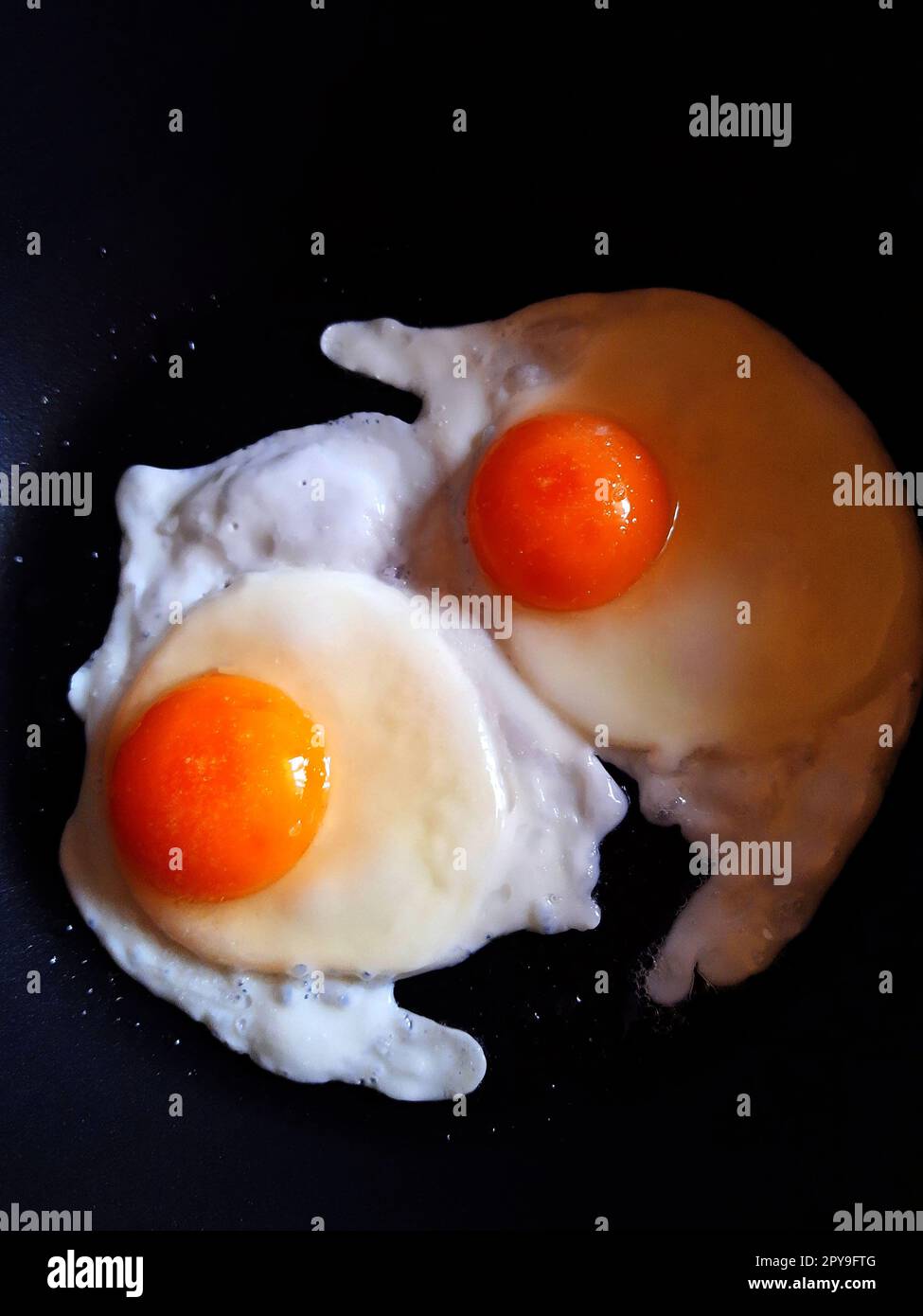 Two fried chicken eggs in a black frying pan close-up Stock Photo - Alamy