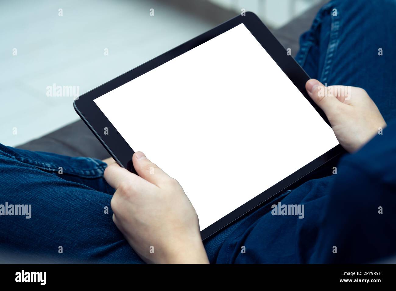Digital tablet computer with blank white screen in male hands, from above view closeup. Young guy work on gadget at home Stock Photo