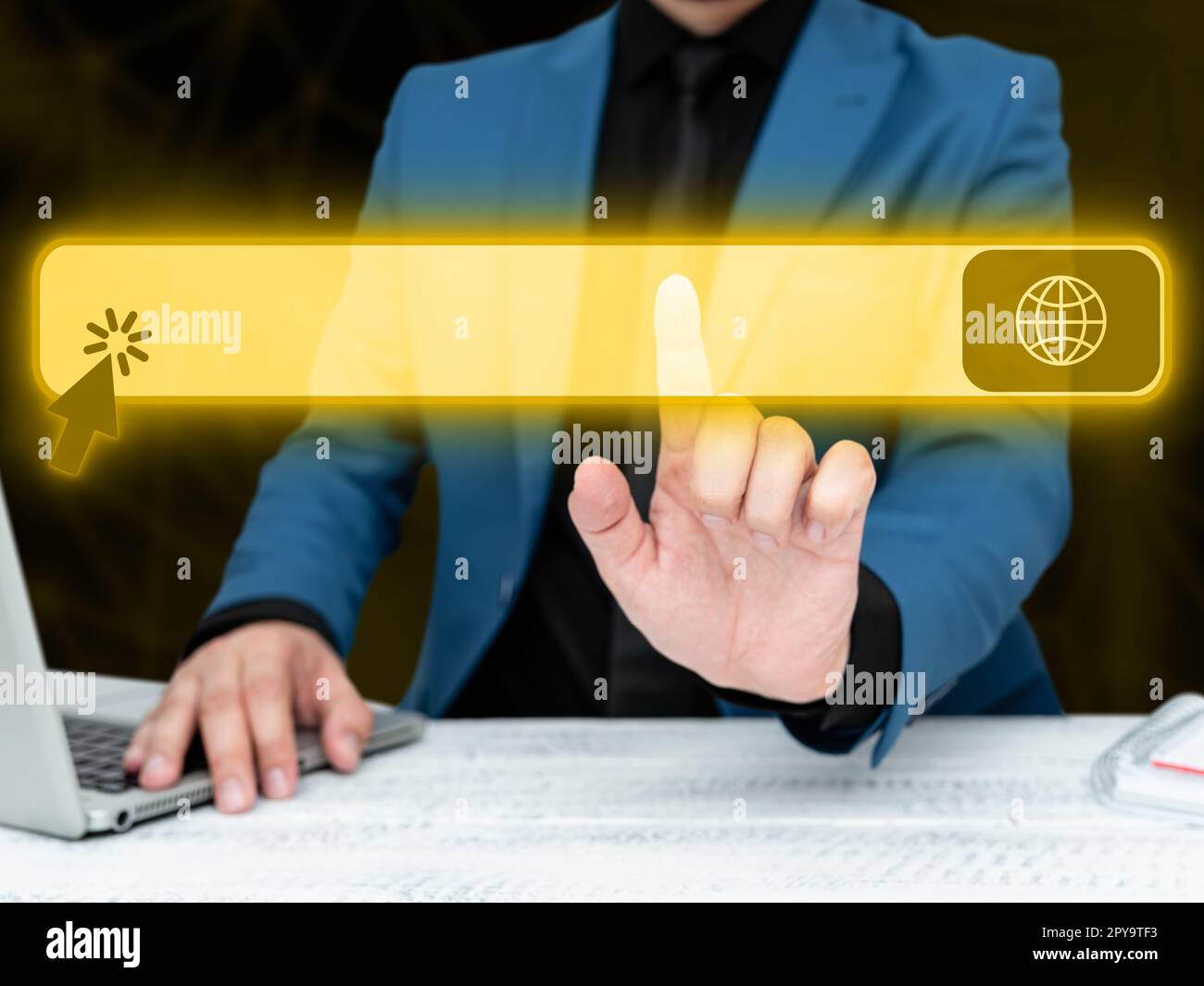 Businessman in blue jacket sitting at the white table and pressing virtual button. Laptop laying on the desk.Futuristic style image with colored glow. Stock Photo