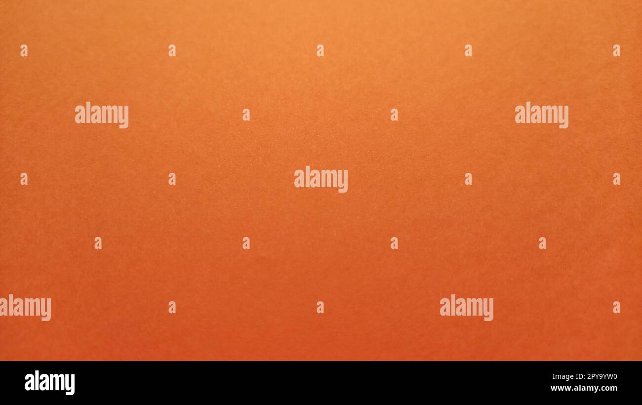 A sheet of thick paper of bright orange color. Close-up. Background intense shade. Natural lateral lighting. Fine cardboard or paper texture. Light gradient in degree of illumination. Copy space Stock Photo