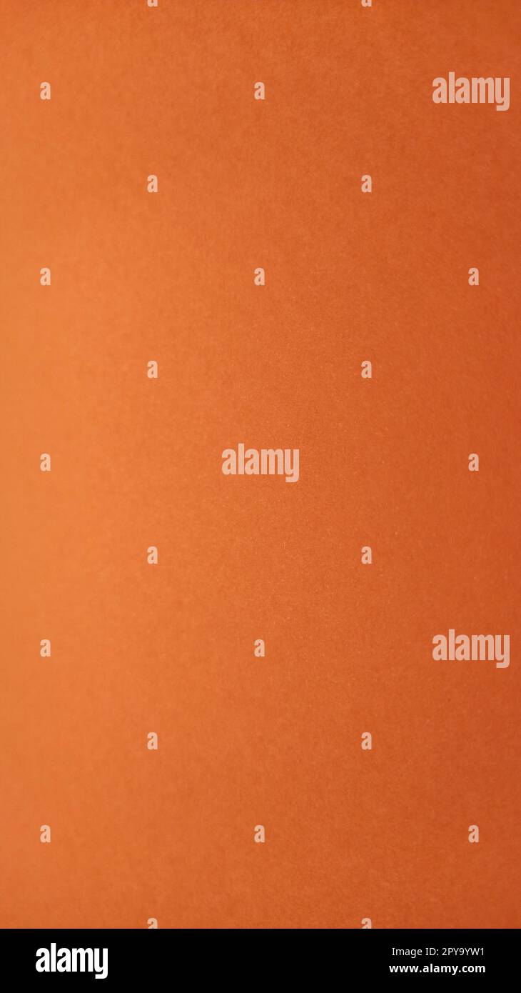 A sheet of thick paper of bright orange color. Close-up. Background intense shade. Natural lateral lighting. Fine cardboard or paper texture. Light gradient in degree of illumination. Vertical image Stock Photo