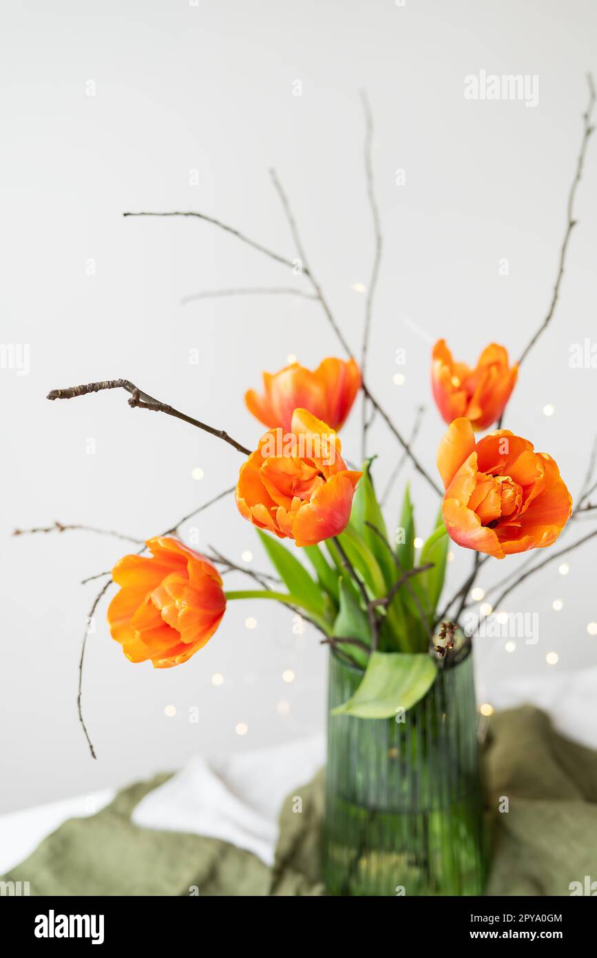 A very beautiful spring bouquet in a green vase stands on a table on a linen tablecloth, orange peony tulips. Stock Photo