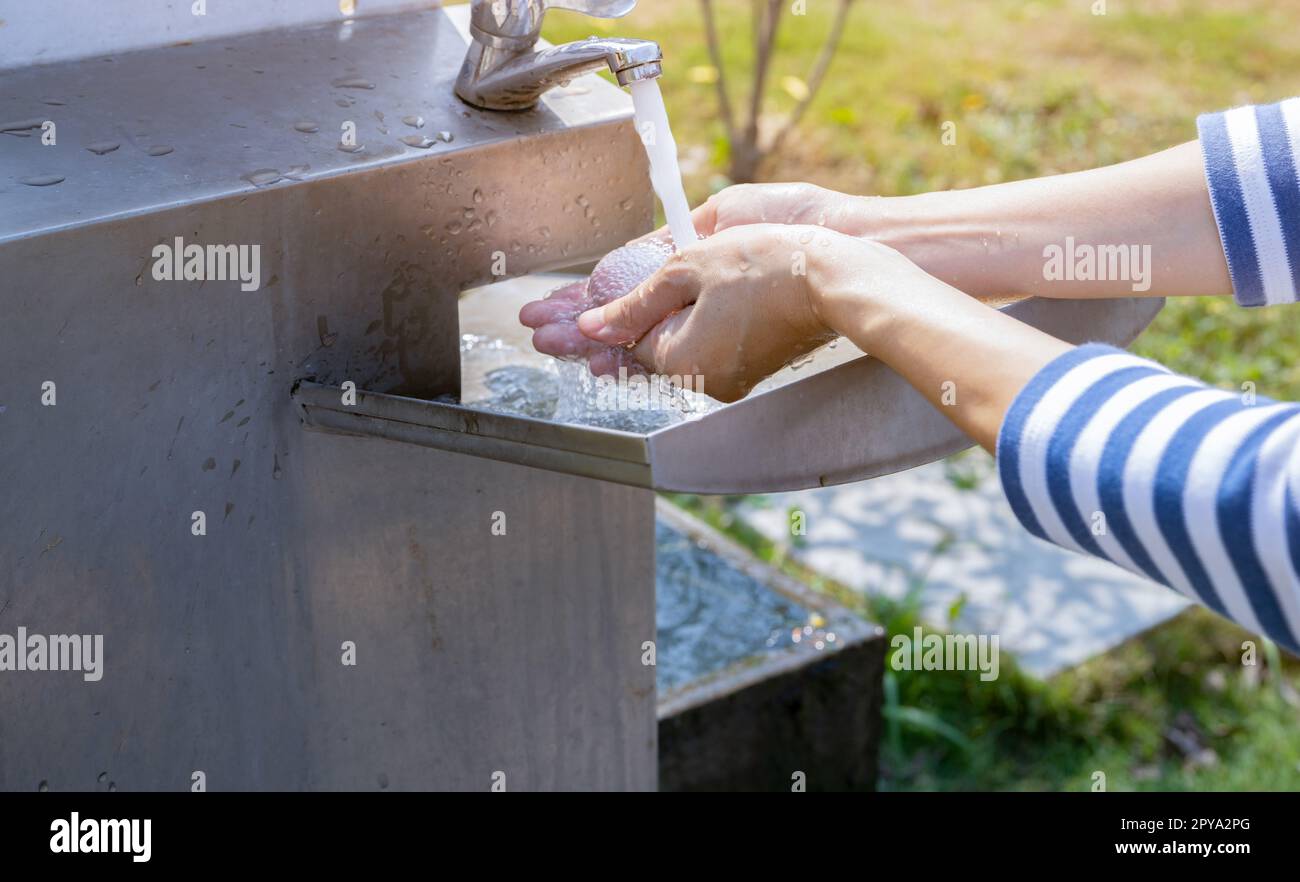 World water day concept. Woman washing hands with tap water under faucet at stainless steel sink. Washing hands with tap water at outdoor sink. Personal hygiene. Water consumption and sustainability. Stock Photo