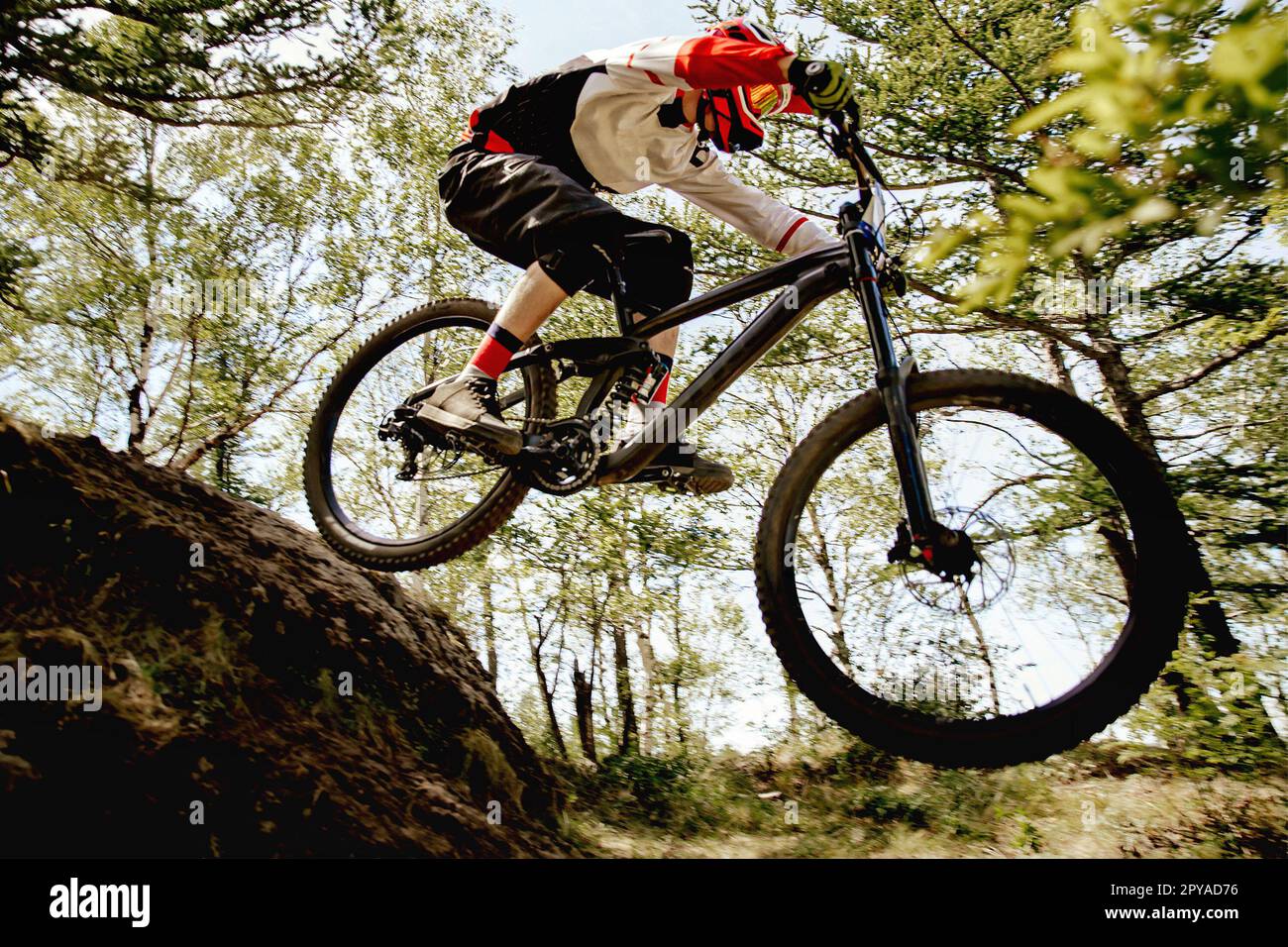 male racer cycling steep descent downhill in forest, summer mountainbike championship Stock Photo