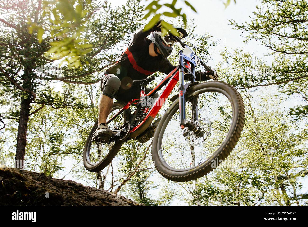 male racer jumping steep descent bottom view, downhill race, summer mountainbike championship Stock Photo