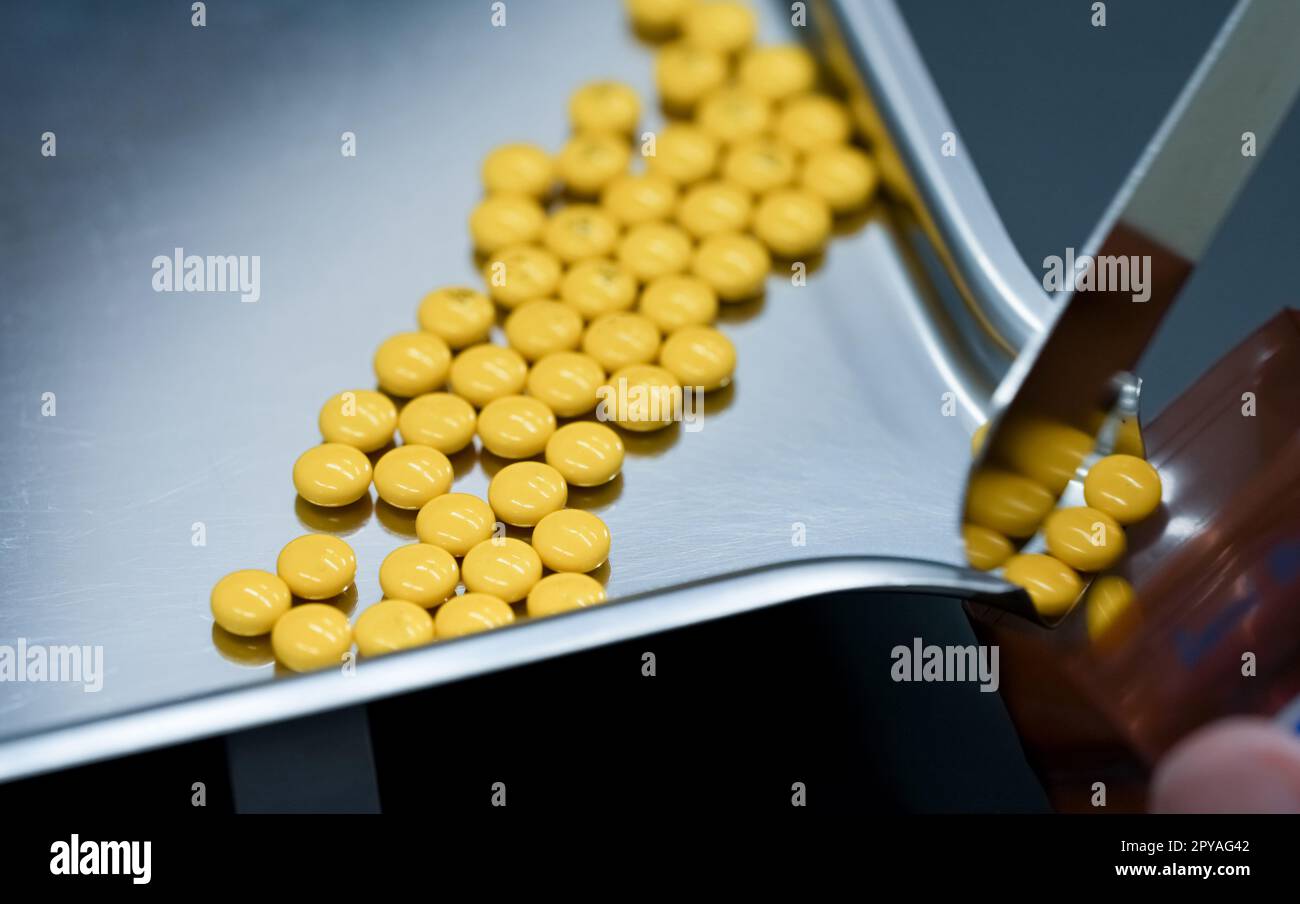 Selective focus on yellow tablets pills on stainless tray with blur hand of pharmacist or pharmacy technician counting pills into a plastic zipper bag. Prescription medicine. Medical health care. Stock Photo