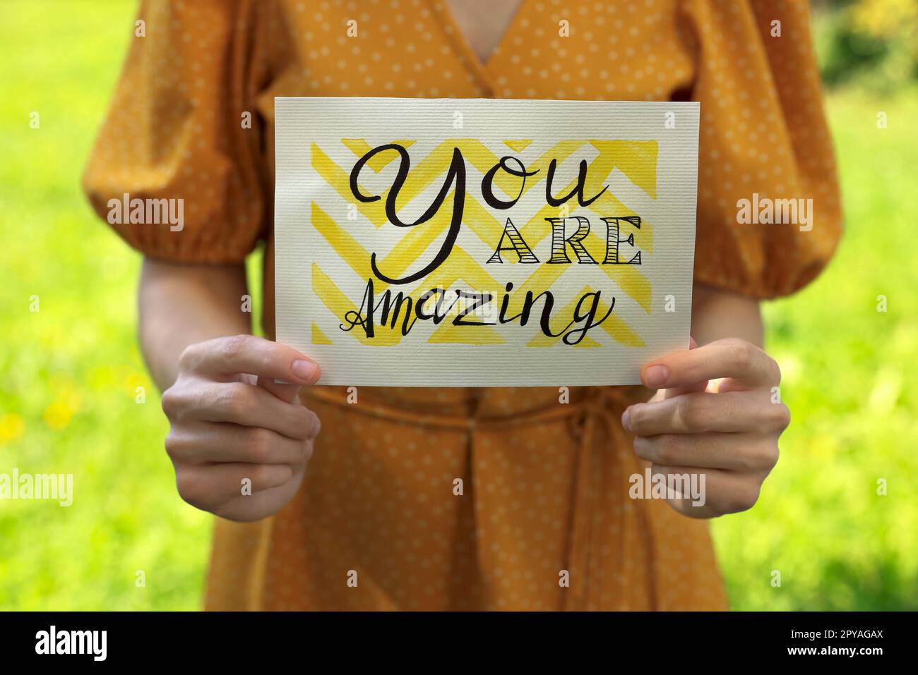 Woman holding card with phrase You Are Amazing outdoors, closeup Stock Photo