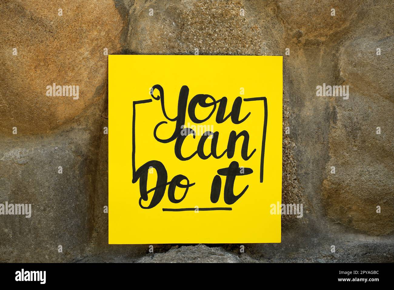 Yellow paper note with phrase You Can Do It on stone background Stock Photo
