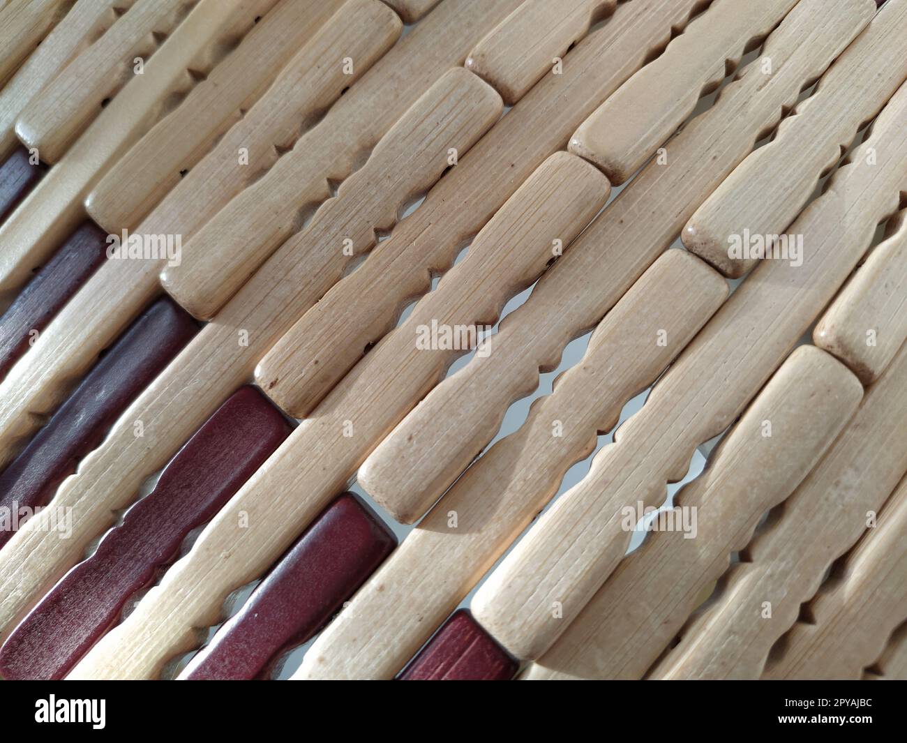 reed or wood mat. The rug is a mat under the hot. Knitted processed wood sticks with rounded edges. Close-up. Yellow, brown and beige colors. Side lighting. Traditional bamboo pad texture Stock Photo