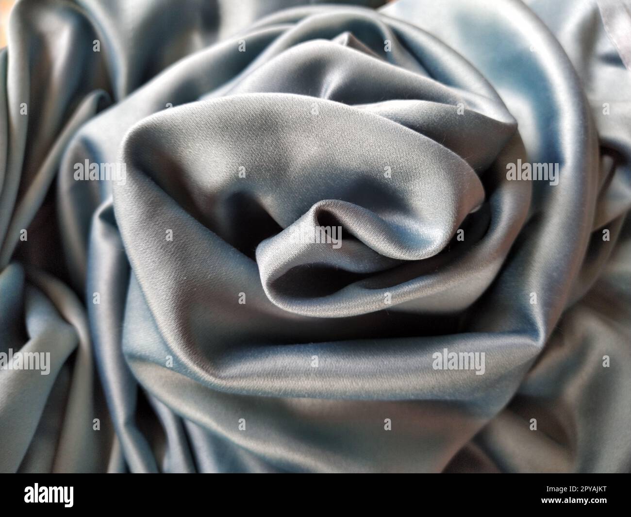 Silky to the touch fabric of gray - blue color with a brilliant shimmer. Natural lighting, light and shadow. The material is casually folded into a circle, resembling a rose bud. Polyester Textile Stock Photo