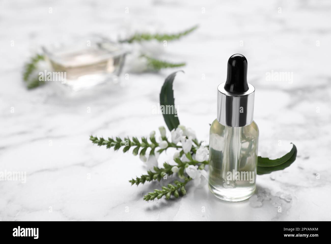Bottle of essential oil and flowers on white marble table, closeup. Space for text Stock Photo