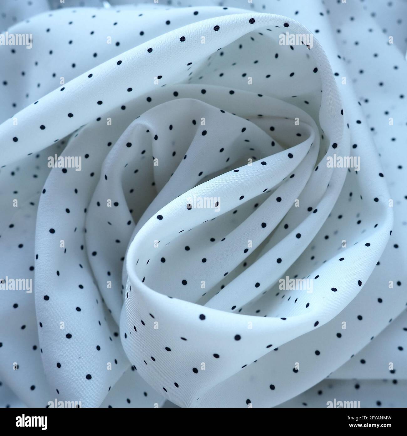 Texture of silk fabric. Black polka dots on a white background. Dress lightweight synthetic fabric in white with a repeating pattern. The textile is made up of waves and folds. Feminine classic style. Stock Photo