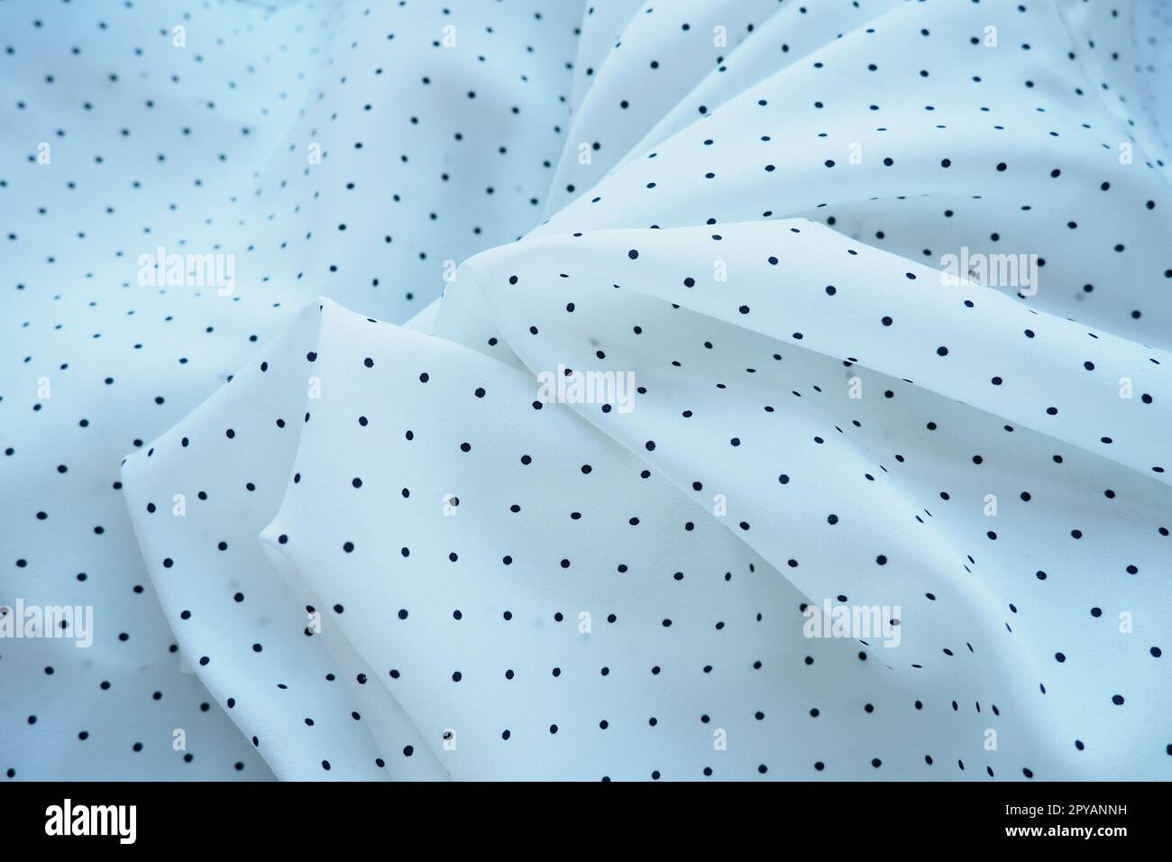Texture of silk fabric. Black polka dots on a white background. Dress lightweight synthetic fabric in white with a repeating pattern. The textile is made up of waves and folds. Feminine classic style. Stock Photo