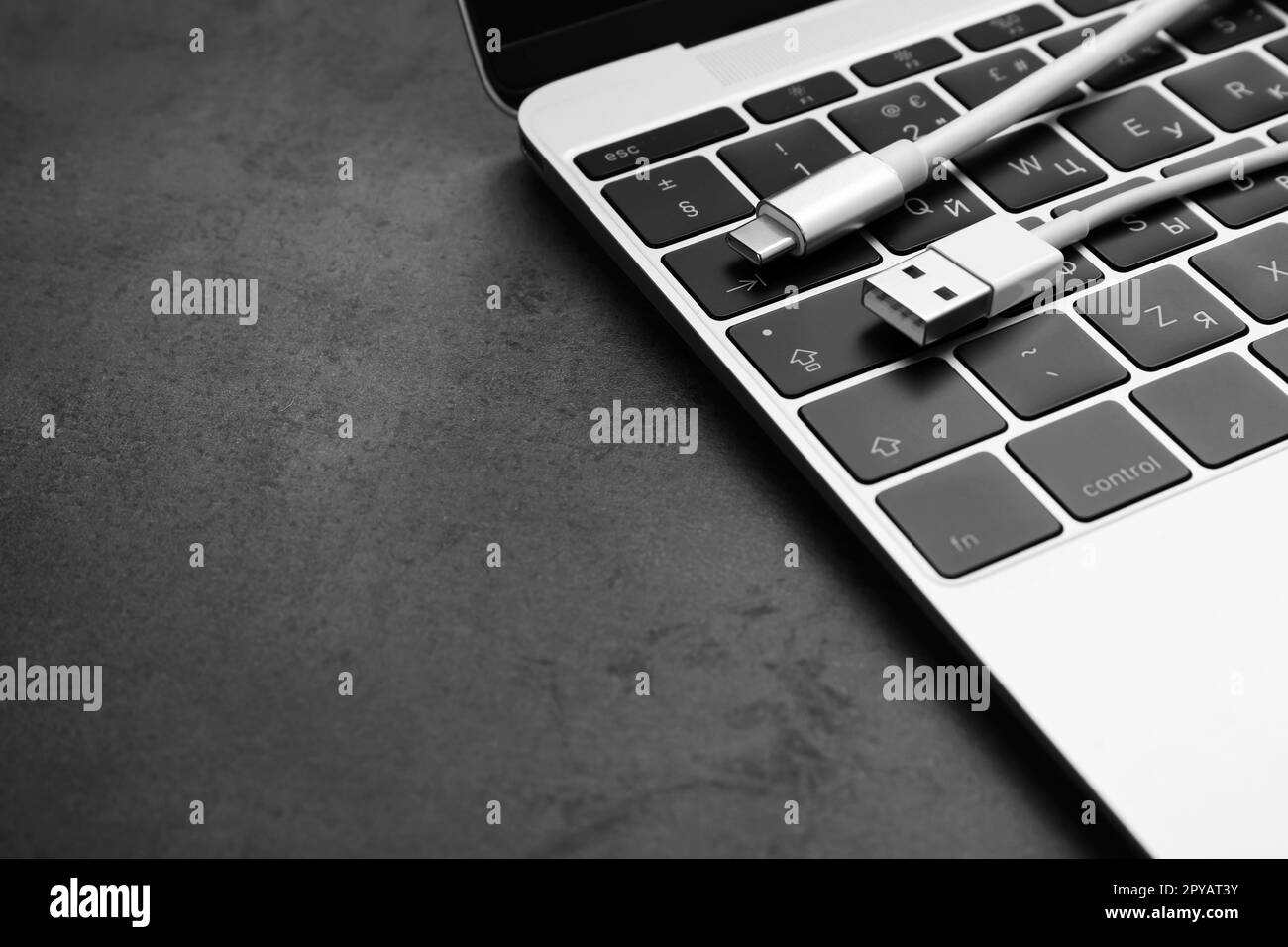 USB cable with type C connector and laptop on dark table, closeup