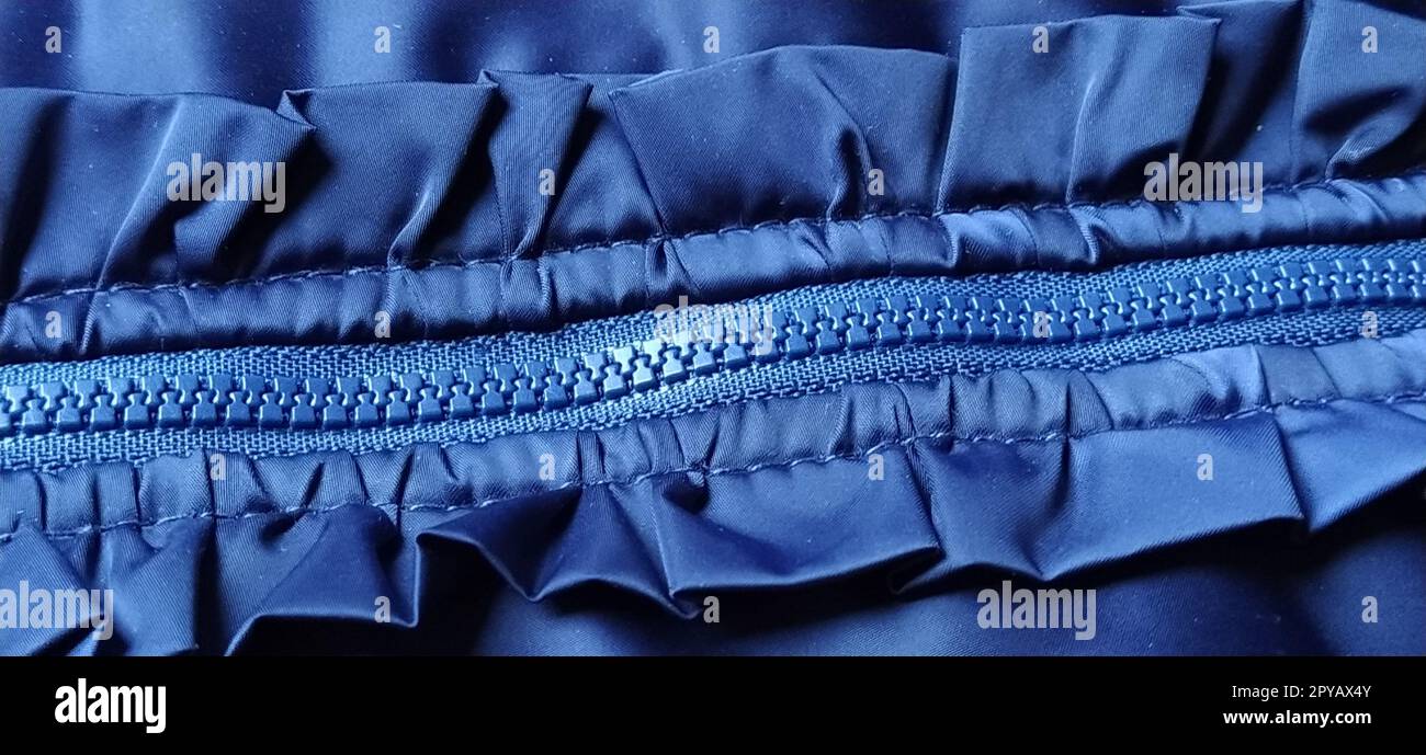 Buttoned zip on a blue raincoat. Waves and folds in the fabric. Beautiful flounces, ruffles, frills. Decorative finishing of a garment. Smocked, sewn silk fabric. Nice casual wear. Banner Stock Photo