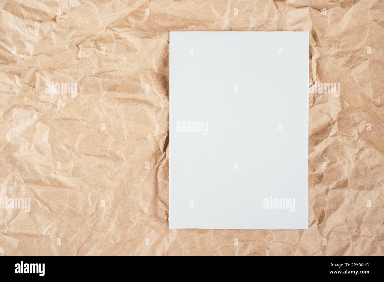 Background image of rough crumpled recycled textured kraft paper with sheet of white cardboard on side. Copy space Stock Photo