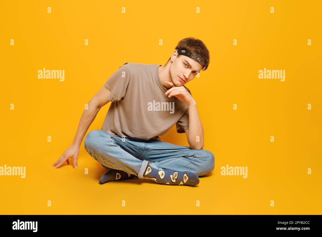 Casual young adult man sitting in a vibrant yellow studio Stock Photo