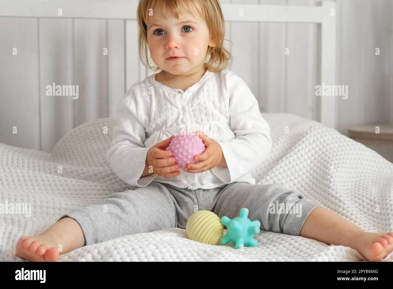 Cute baby girl playing tactile knobby balls. Young child hand plays