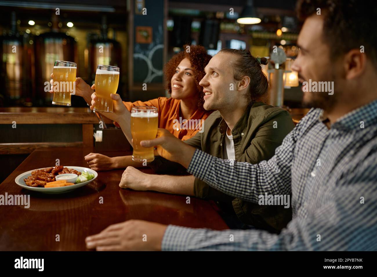 Cheerful friends drinking draft beer at bar table in pub Stock Photo
