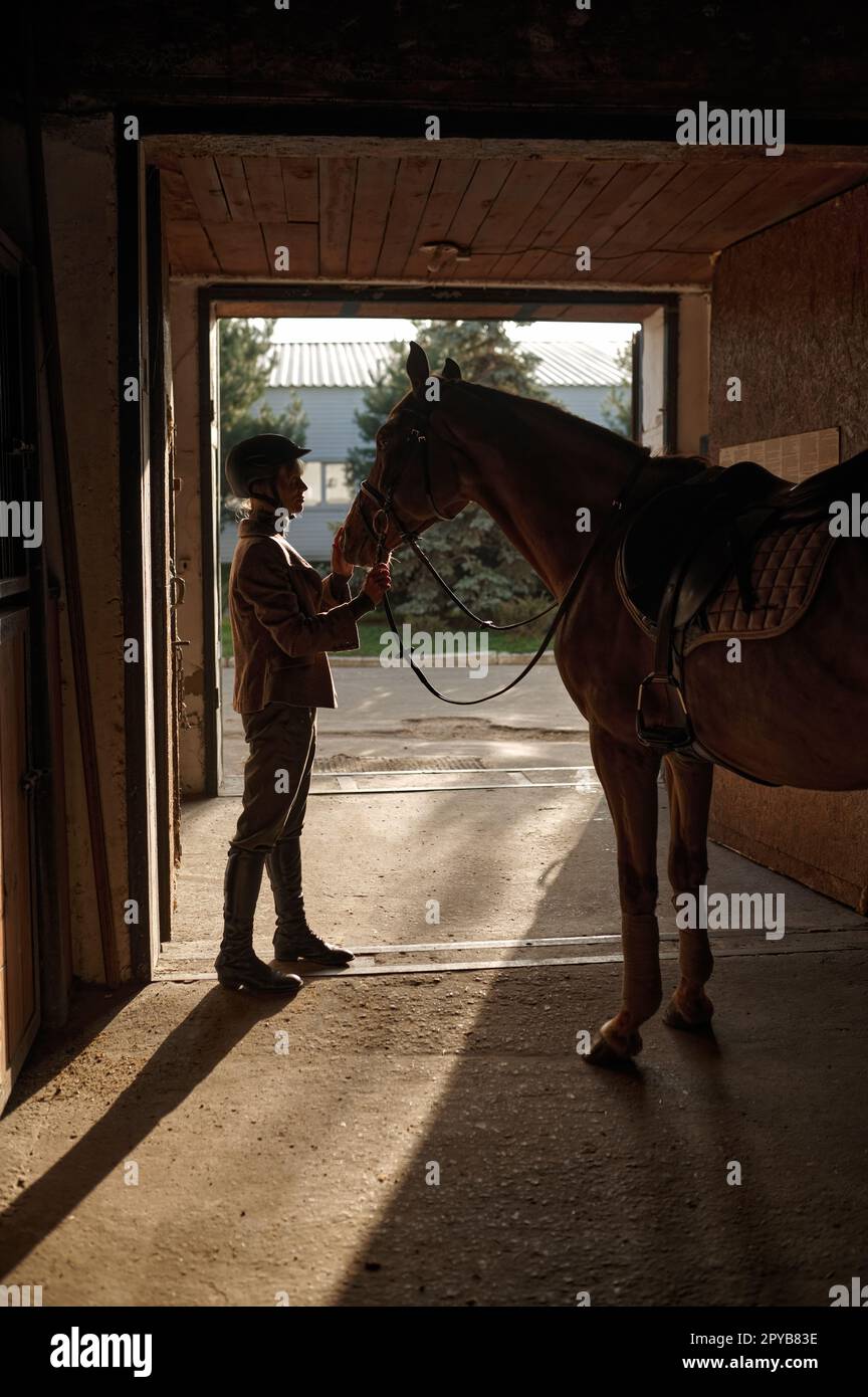 Woman caressing her horse while standing over stable gate Stock Photo