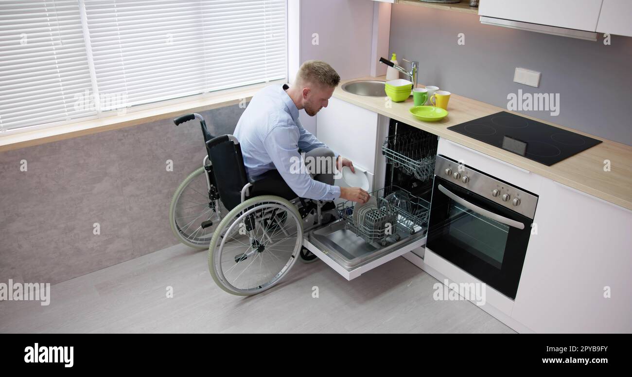 Person With Disability In Wheelchair Using Dishwasher In Kitchen Stock