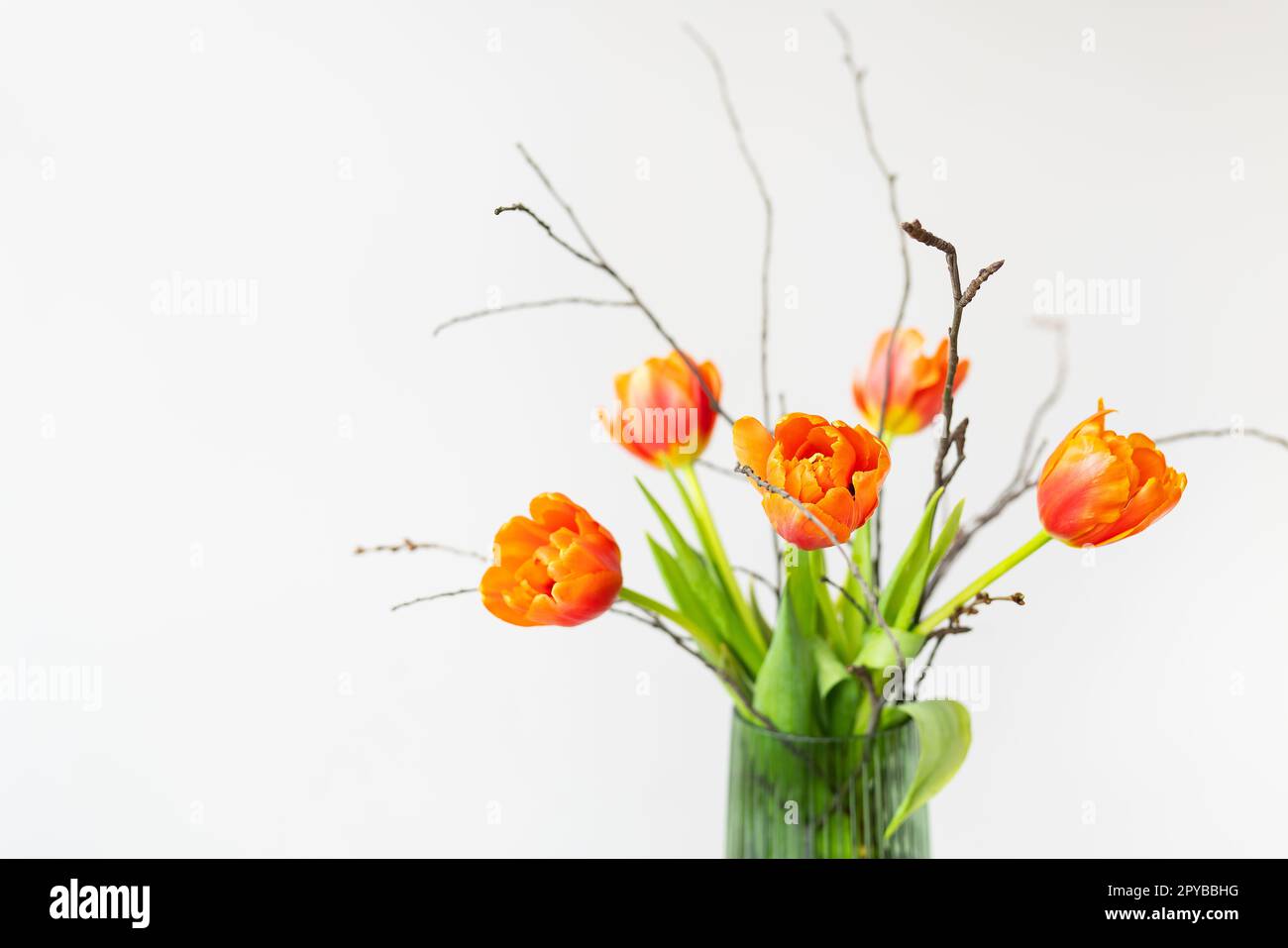 A very beautiful spring bouquet in a green vase stands on a table on a linen tablecloth, orange peony tulips. Mother's Day, March 8, Valentine's Day. Place for an inscription. Stock Photo
