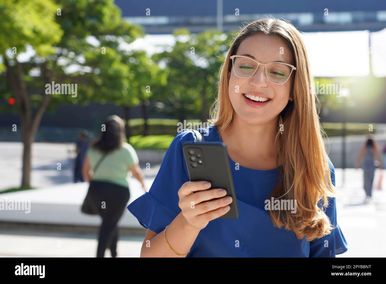 Young lady with glasses checking her mobile phone outdoors Stock Photo