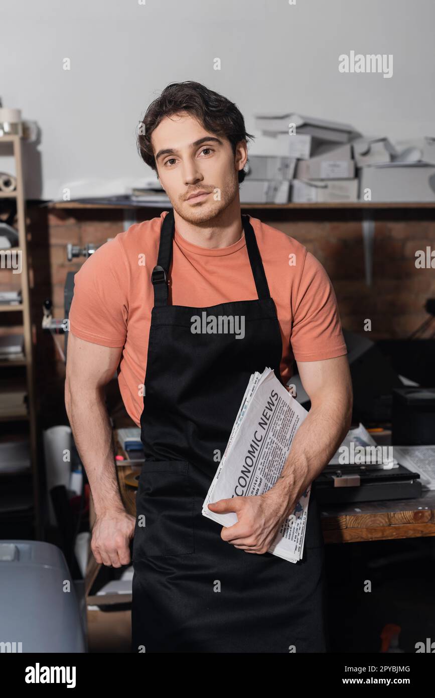 young typographer in apron holding newspapers with economic news,stock image Stock Photo