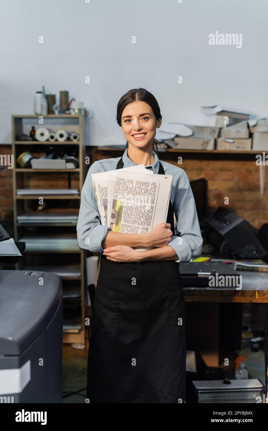 overjoyed typographer in apron holding freshly printed newspapers,stock image Stock Photo