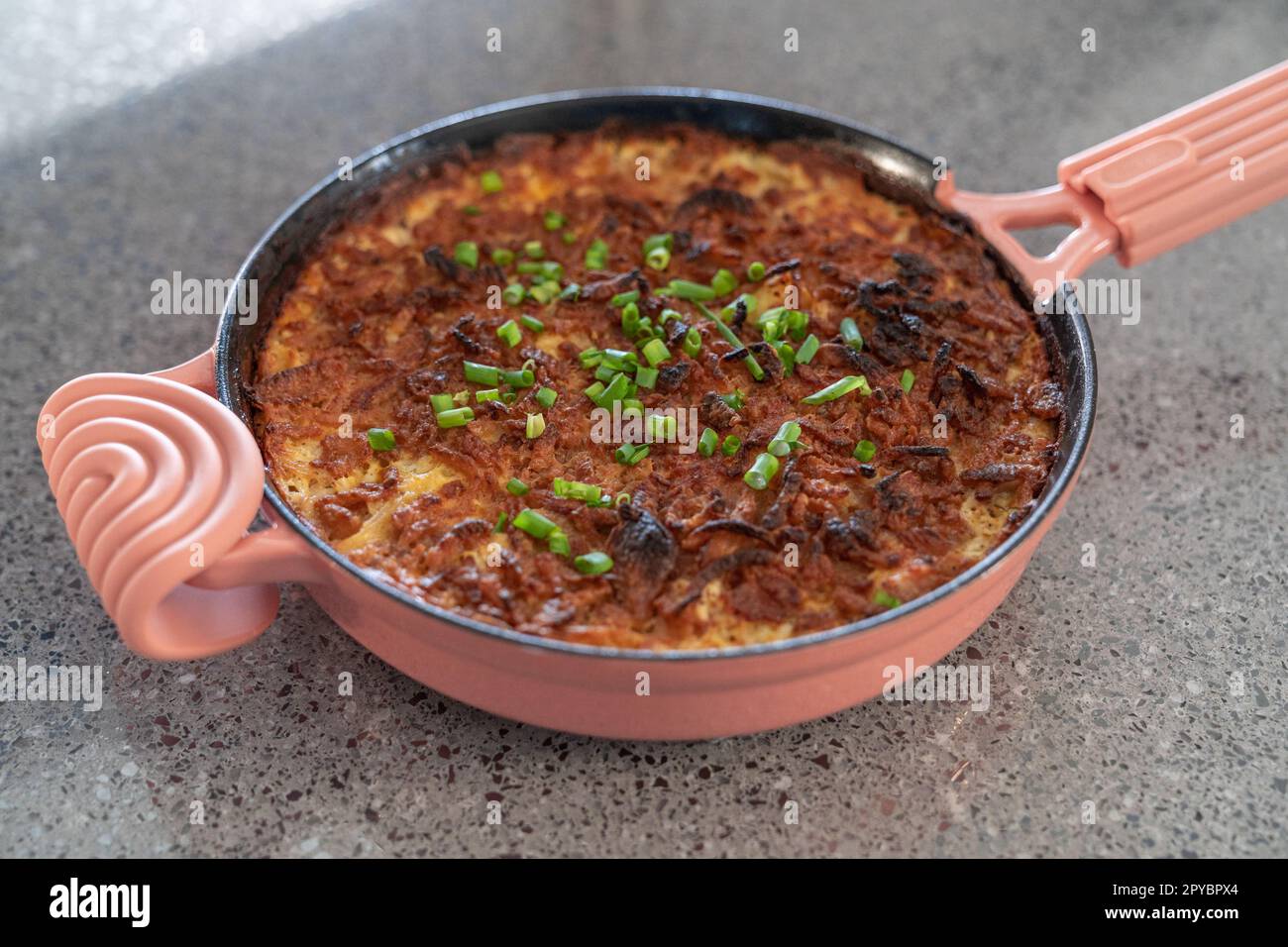 Pink cast iron skillet casserole dish with cheese and green onions. Wide Shot. Stock Photo