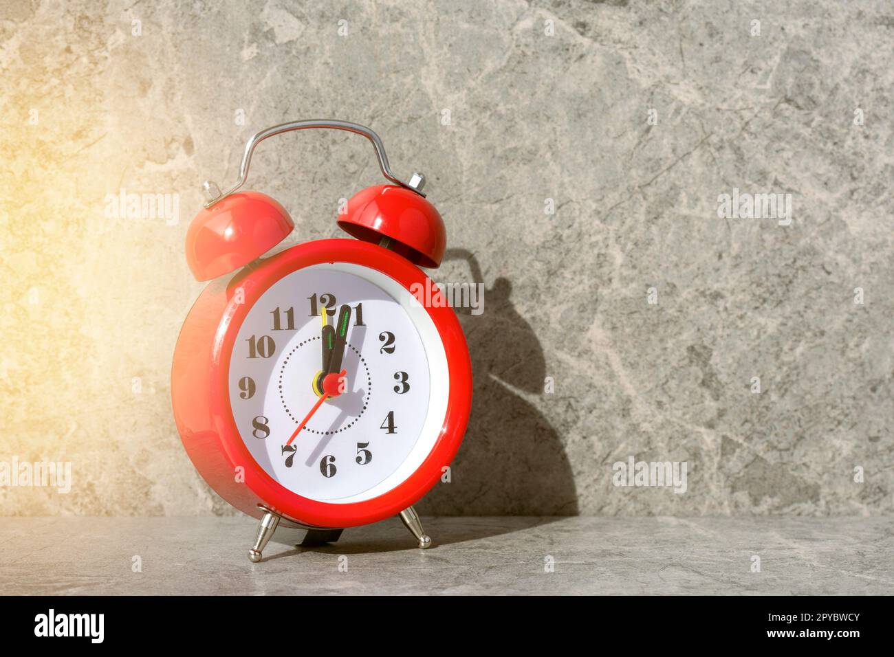 Red alarm clock with a sunlight and shadow on the grey stone background Stock Photo
