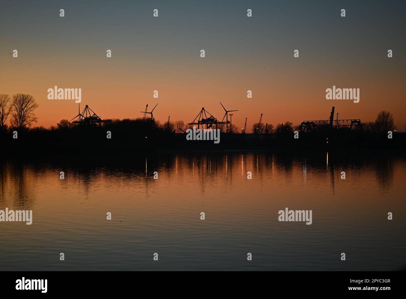 Evening mood besides a river against a containerport and sunset Stock Photo