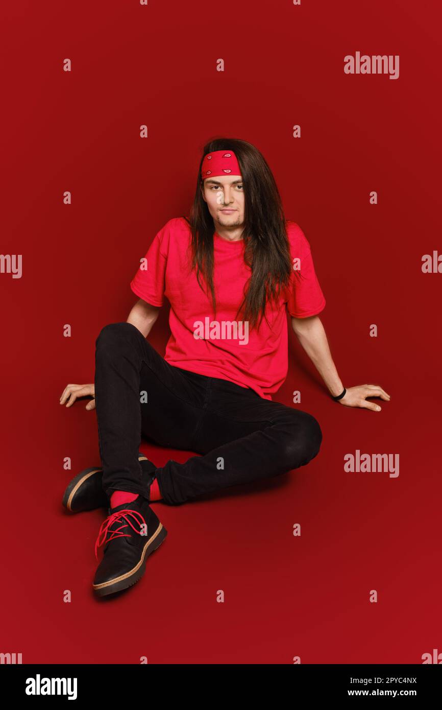 Man with long hair sitting on floor in red studio Stock Photo