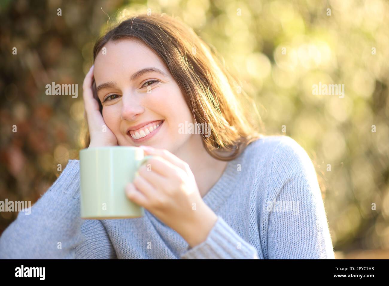 Happy woman looks at camera holding coffee cup Stock Photo