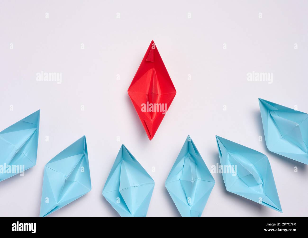 A group of blue paper boats surrounded one red boat, the concept of bullying, search for compromise. Top view Stock Photo