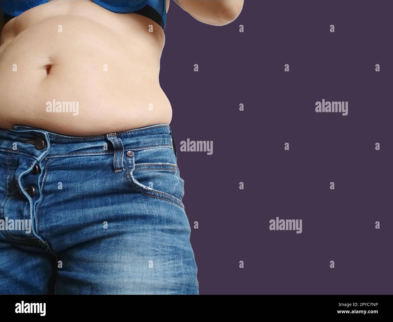 Saggy belly. Folds of leather and fat on the side hanging over the waist of the jeans. A figure overeating or pregnancy. Obesity and Diabetes. Velvet violet background. Cellulite flabby muscles. Stock Photo